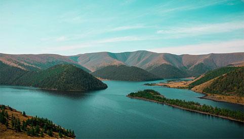 Mountain lake with forested headlands and surrounding Khangai ridges.