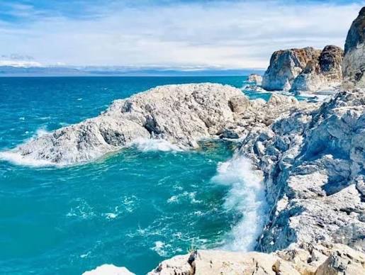 Blue lake waves breaking against pale rocky shores.