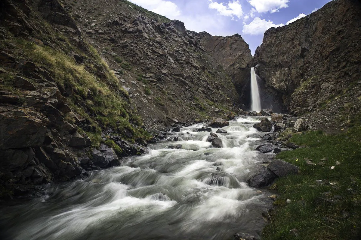 Waterfall between rocky gorge walls, with a stream cascading over boulders.