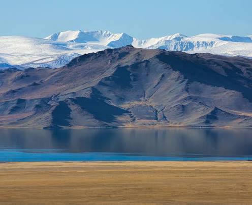 Blue lake beneath bare mountain ridges and snowy distant peaks.